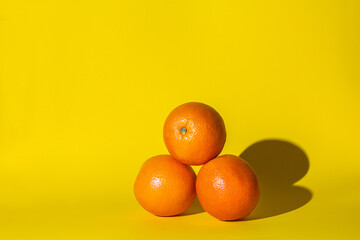 oranges fruits citrus ,three objects,hard shadow,orange color round,lie on the surface of the yellow background.concept juice vitamins.