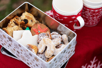 Tin of assorted homemade Christmas cookies and cakes next to two empty mugs