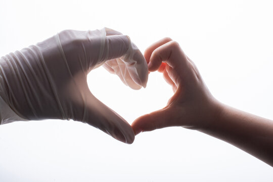Close-up of a person wearing a latex glove making a heart shape with a person not wearing a glove