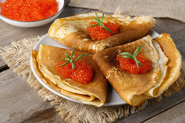 Stack of russian thin pancakes blini with red caviar on an old wooden table. Maslenitsa, traditional Russian blini