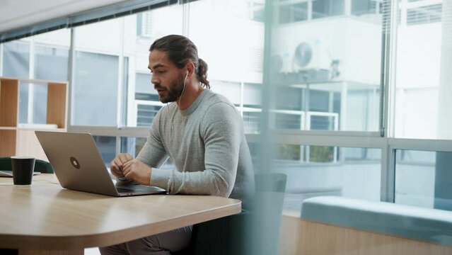 Business man having a virtual meeting on a laptop, sitting in a modern coworking office. Young business professional using technology to communicate with his colleagues while working remotely.