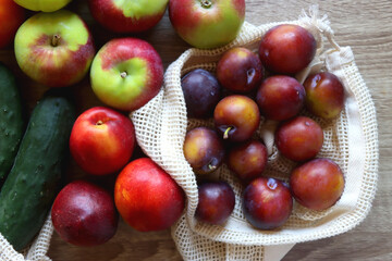 Straw bag and reusable fabric bags filled with various healthy fruit and vegetables. Wooden background, top view.