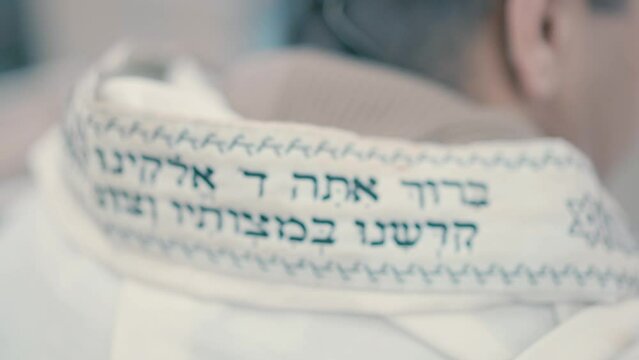 A close-up video shot from the back of a Jewish man praying in a synagogue.