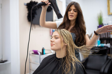 Hairdresser blow drying female customers hair in hair salon.