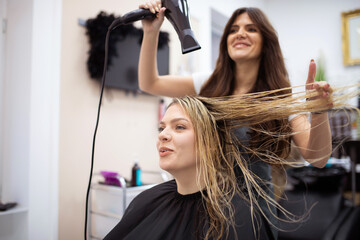 Hairdresser blow drying female customers hair in hair salon.