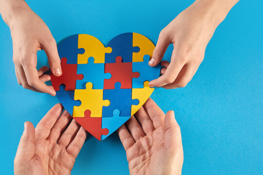 Father and autistic son hands holding jigsaw puzzle heart shape. World Autism Awareness Day