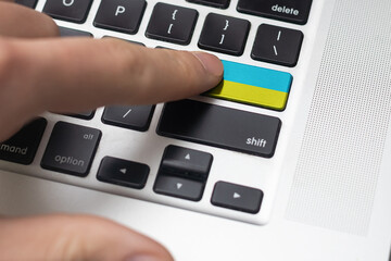 Pressing enter button with Ukraine flag, represents a cyber-attack of Ukraine, metaphor of learning Ukrainian language, black keyboard close up, front view, selective focus.