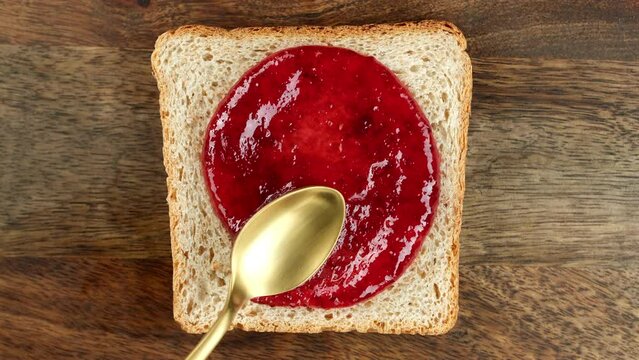 Raspberry jam spreading on bread with a golden spoon, top view. Perfect traditional breakfast
