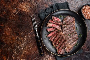 Barbecue denver strip beef meat steak on a plate. Dark background. Top view. Copy space
