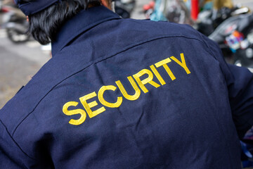 A security guard from behind with a blue jacket and the word security in yellow. Close up on a...