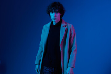 Male model in fashion coat on dark blue background, neon light, style and trends, mixed light, men's fashion