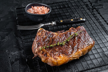 Grilled Striploin beef meat steak or new york steak on a grill rack. Black background. Top view