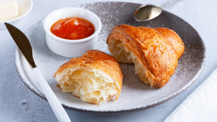 A freshly baked French Croissant, butter and jam.