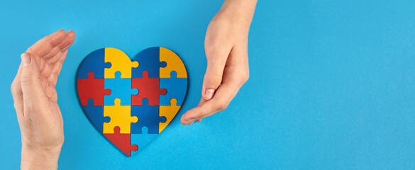 Father and autistic son hands holding jigsaw puzzle heart shape. World Autism Awareness Day
