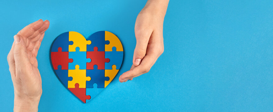 Father and autistic son hands holding jigsaw puzzle heart shape. World Autism Awareness Day
