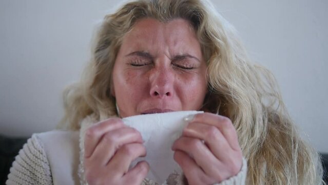 Close-up of a sick woman sneezing into a tissue.