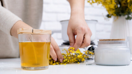 Woman making decorative aroma candle at table with mimosa, closeup
