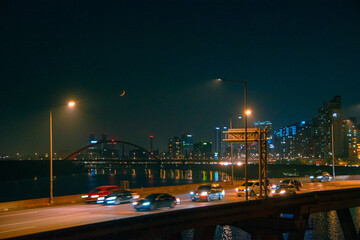 Fototapeta na wymiar night traffic at night at seoul city with a crescent moon view over than river