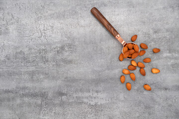 Almond in spoon and group of almond nuts on stone texture background. Top view.
