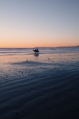People riding horses on the beach at sunset in California