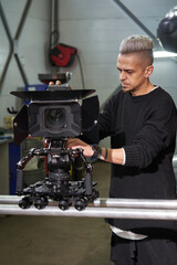 a young caucasian male cameraman is carrying a professional movie camera along the operator's rails on a trolley on a film set
