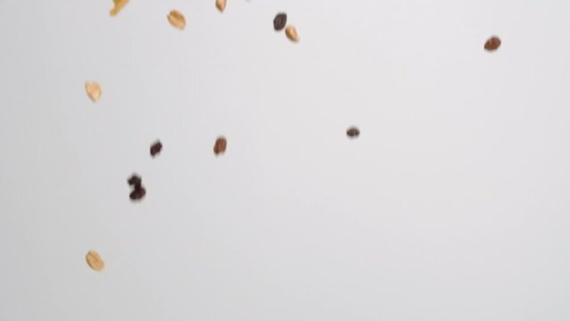 Sweet and salty tropical trail mix with dried fruit slices, coconut, raisins and nuts raining down on white backdrop in slow motion