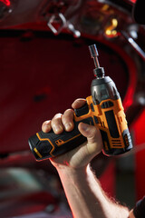 The hand of a caucasian man holds a cordless wrench against the background of a metal part