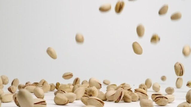 Whole pistachio nuts in shells falling onto white table top and bouncing around in slow motion