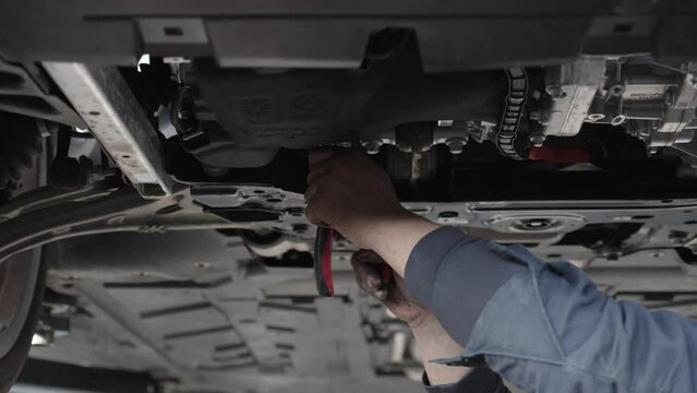 A mechanic under a car uses pliers