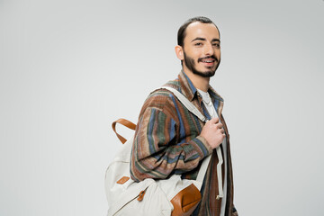 smiling bearded student in colorful shirt standing with backpack isolated on grey.