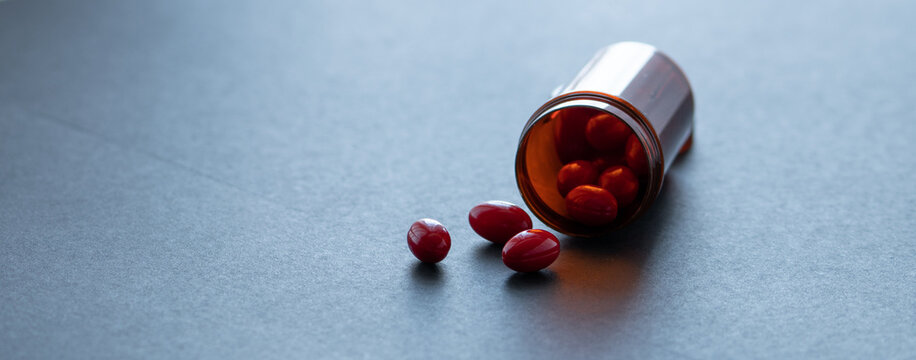 Red capsule pills and brown plastic bottle on dark background. Pharmacy banner. Prescription drugs. Health care and medicine. Pharmaceutical industry. Vitamin and supplement concept. Dose recommended.