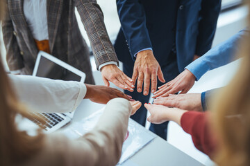 Obraz premium A high-angle shot of a group of male and female colleagues putting their hands together in an office. They are dressed in fashionable business clothes. Their faces are not visible, only their arms. 