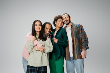 Fototapeta premium cheerful multicultural friends in stylish casual attire embracing while posing isolated on grey.