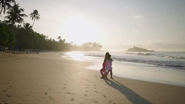 Young happy couple holding hands and running and fooling around on the beach together enjoying summer back view. Boyfriend rasing and spinning girlfriend having fun at the seaside at sunrise.