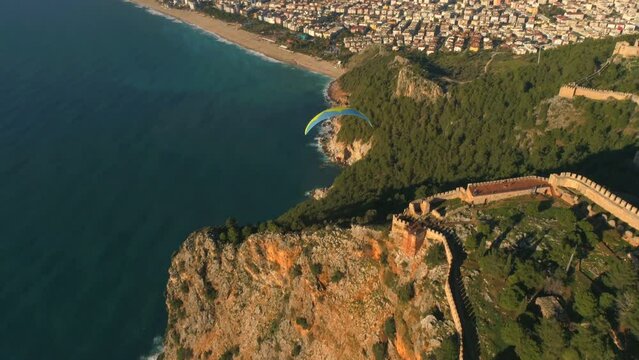 Parachute jumper is flying over beautiful panorama of sunny Alanya town, famous Fortress and mountains overwashed by Mediterranean sea. Drone footage, 4k.