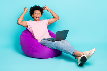 Full length photo of young overjoyed it developer man fists up done best project freelancer sit pouf laptop isolated on aquamarine color background