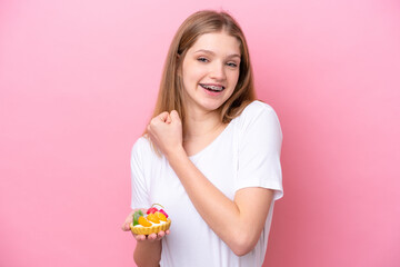 Teenager Russian girl holding a tartlet isolated on pink background celebrating a victory