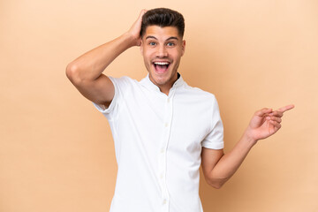 Young caucasian man isolated on beige background surprised and pointing finger to the side