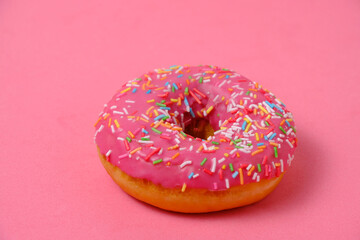 Donut with pink icing and multicolored sugar sprinkles.On pink background.