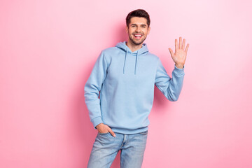 Photo of sweet friendly man wear blue hoodie smiling waving arm palm smiling isolated pink color background © deagreez