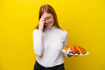 Young redhead woman holding waffles isolated on yellow background laughing
