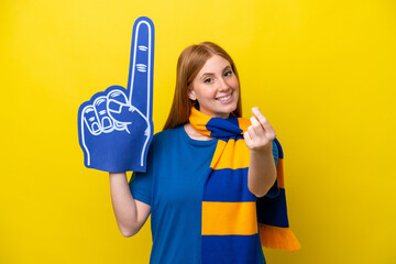 Young redhead sports fan woman isolated on yellow background making money gesture