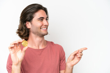Young handsome man holding a Bitcoin isolated on white background pointing to the side to present a product