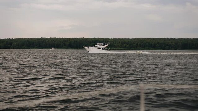 A boat is moving along the water surface of the lake. The coastline and the forest are visible behind it.