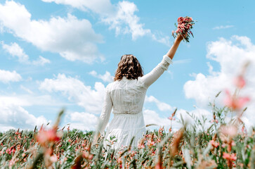Back view of woman in white dress holding up a flower bouquet in a flower field