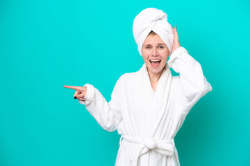 Young woman in a bathrobe isolated on blue background surprised and pointing finger to the side