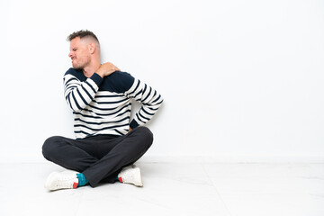 Young man sitting on the floor isolated on white background suffering from pain in shoulder for having made an effort