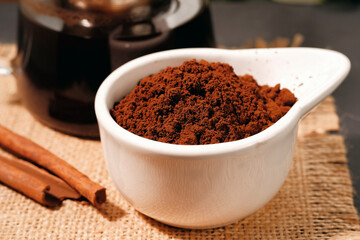 Coffee grounds in a bowl with cinnamon sticks on a burlap napkin