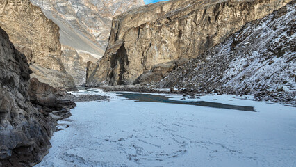A frozen glass-like Zanskar river with dramatic Himalayan mountains on either side, in peak indian winters