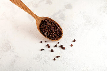 Cacao nibs in wooden spoon on grey surface, close-up. Sugar-free product. Natural antidepressant....